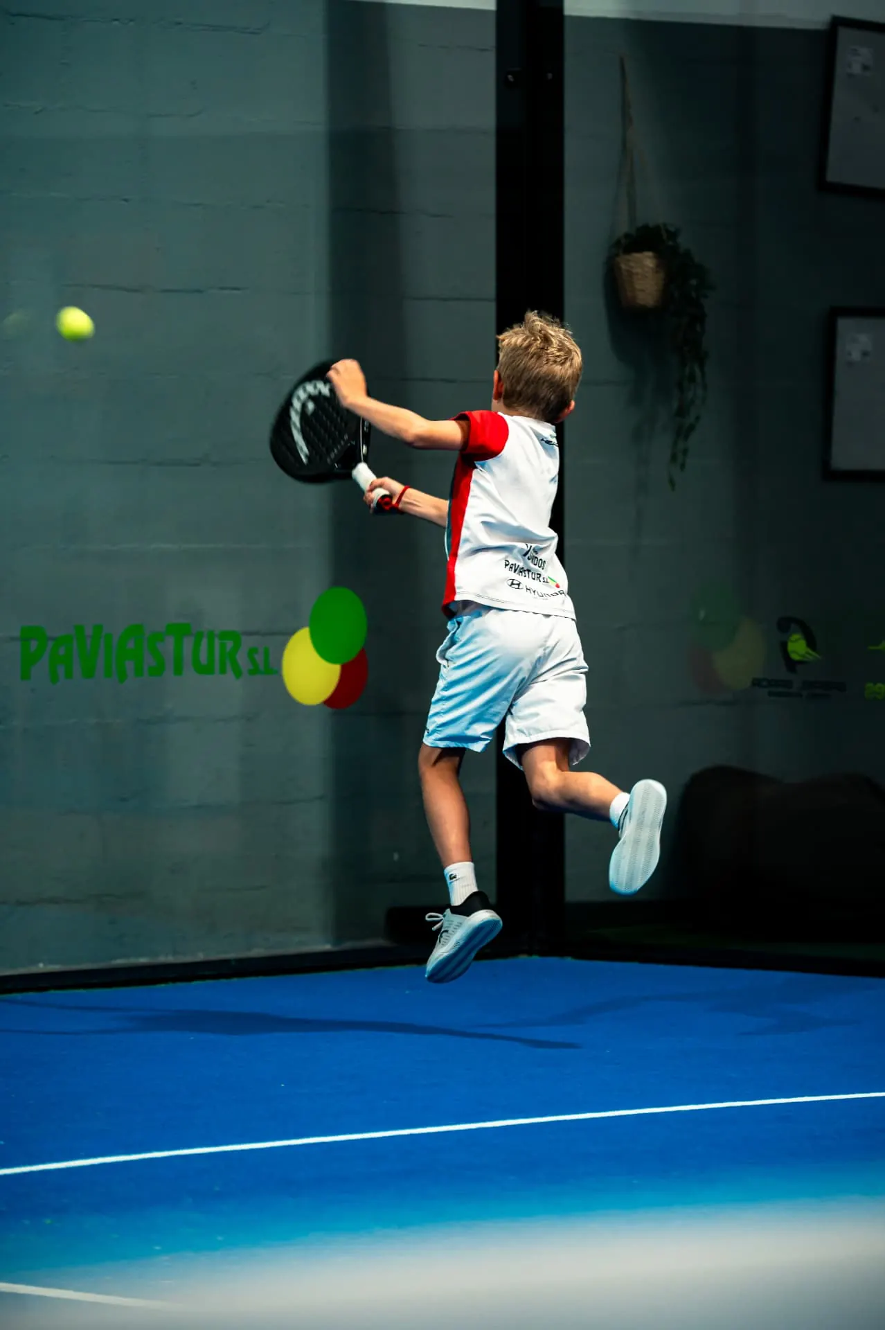 Niño saltando para golpear la bola en una pista de pádel